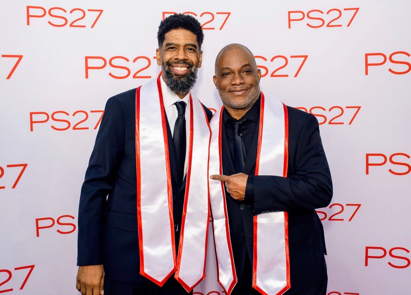 Troy and Mo in dark suits with white and crimson stoles on the PS27 red carpet